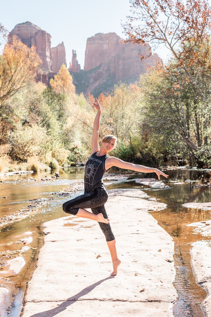A woman gracefully performs yoga in a picturesque canyon setting with autumn foliage.